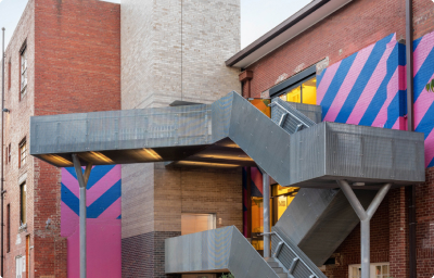 A brick 3-storey building with an external steel staircase and a blue and pink mural
